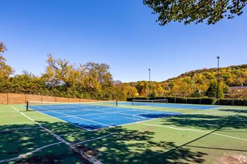 Two tennis courts with trees in the background on a sunny day